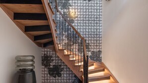Una escalera de madera con barandilla de metal que conduce a un cuarto con papel tapiz estampado y una escultura moderna.