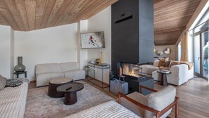 Una sala de estar moderna con chimenea, techo de madera y ventanas amplias.