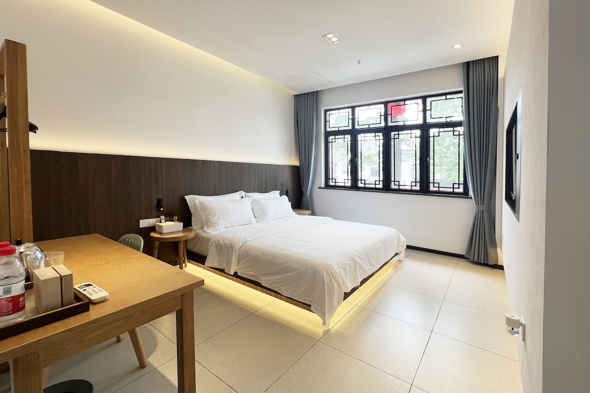 A hotel room with a bed, bedside table, and a desk with a chair.