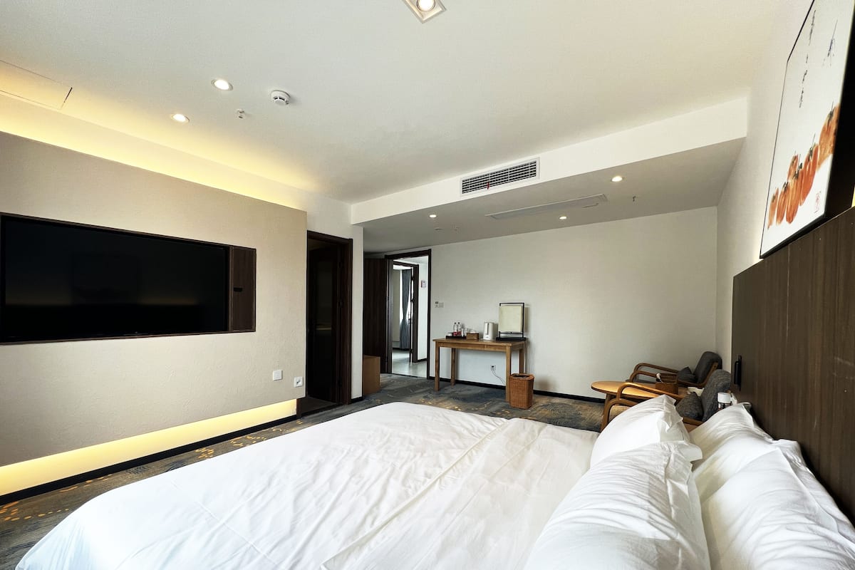 A hotel room with a large bed, a desk with a chair, a television mounted on the wall, and a large window.