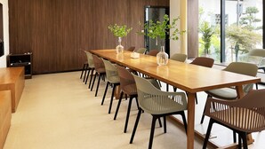 Un salón de conferencias con una larga mesa de madera, varias sillas y dos plantas en macetas.