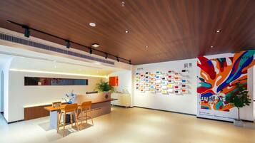 A modern reception area with a wooden ceiling, a reception desk, chairs, a potted plant, and a wall displaying color samples.