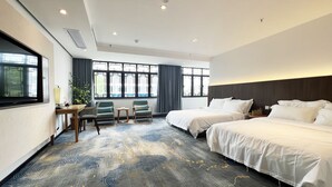 Habitación de hotel con dos camas, un escritorio con silla, televisión y ventanas amplias con cortinas.