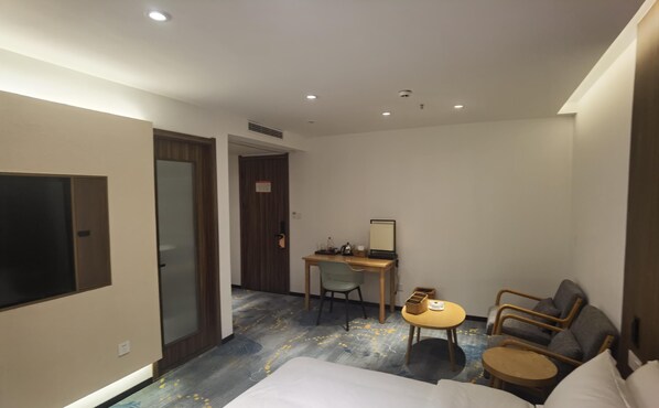 Quarto de hotel com uma cama, uma secretária com cadeira, uma mesinha com cadeira e uma televisão na parede.