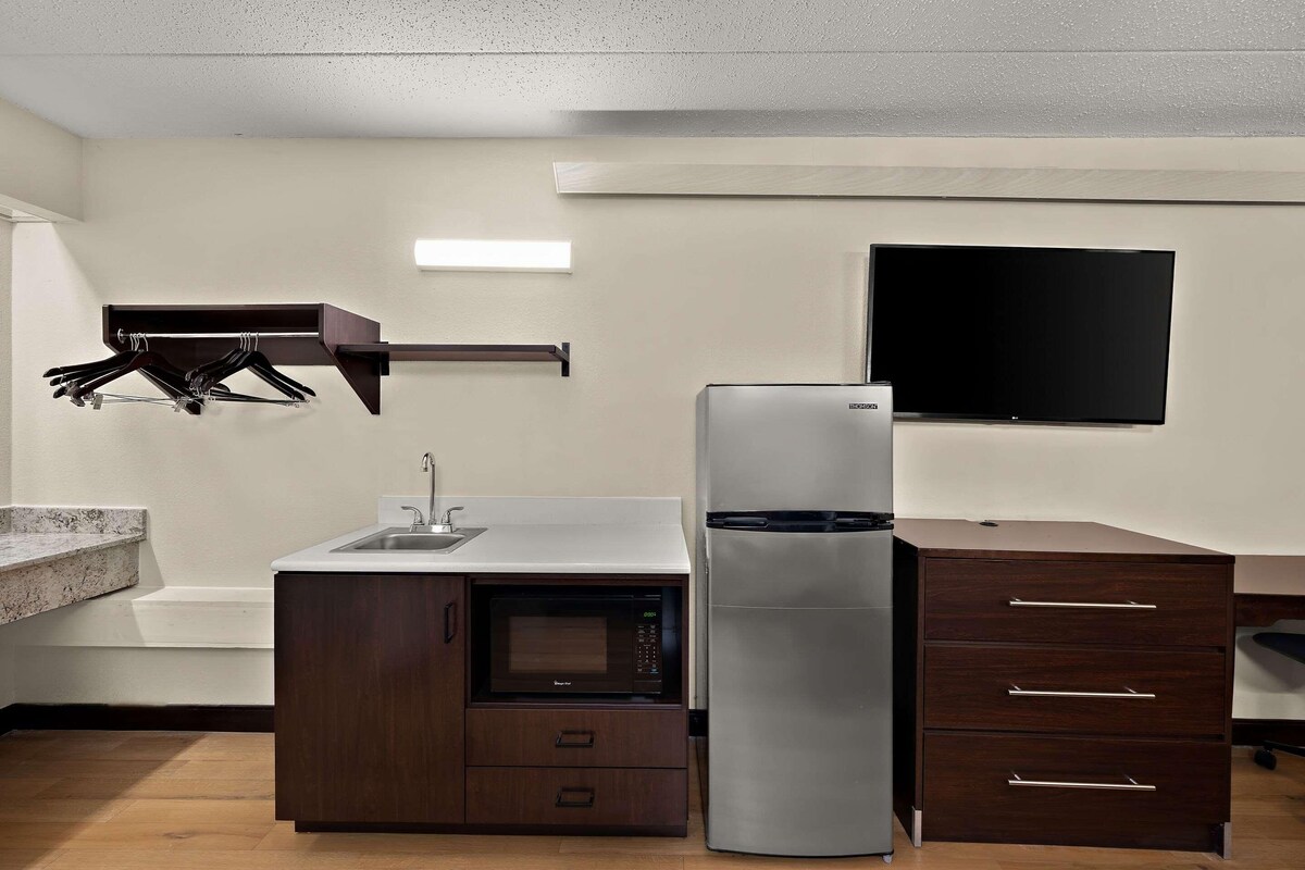 A compact kitchen with a built-in microwave, a refrigerator, a sink, and a wooden cabinet.