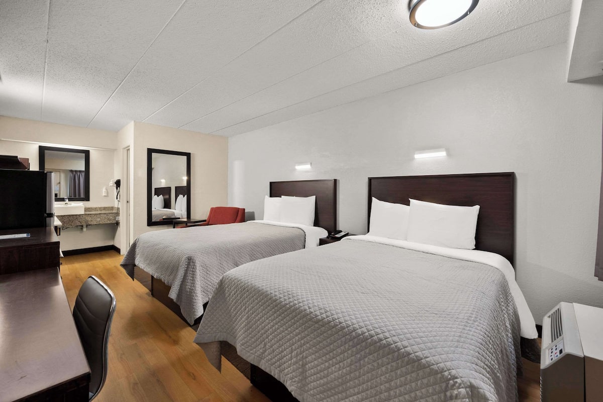 Habitación de hotel con dos camas, un escritorio, una silla, un televisor y un espejo.