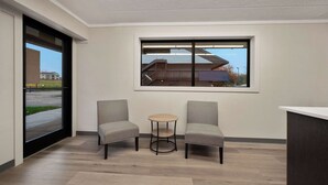 Un espace d’accueil comprenant deux fauteuils, une petite table ronde et une grande fenêtre donnant sur un immeuble et un parking.