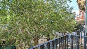 A balcony with a wrought iron railing overlooking a street with trees and a building with a balcony.
