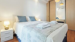 A neatly made bed with a patterned bedspread, a bedside lamp, and a wooden wardrobe with a mirror.