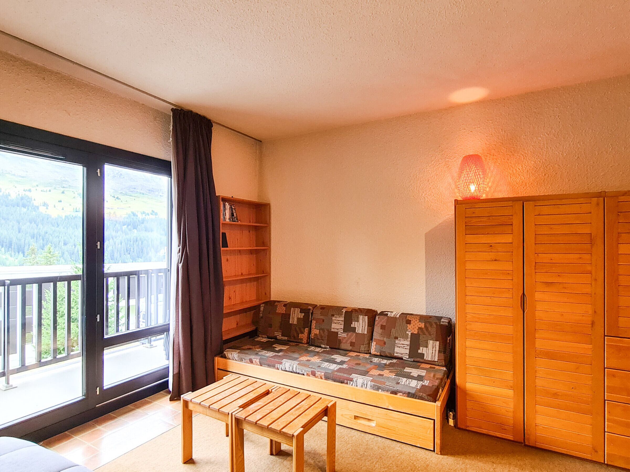 Een kamer met een houten bankje, een klein tafeltje, een bank met een gestreept kussen, een houten garderobe en een boekenkast.