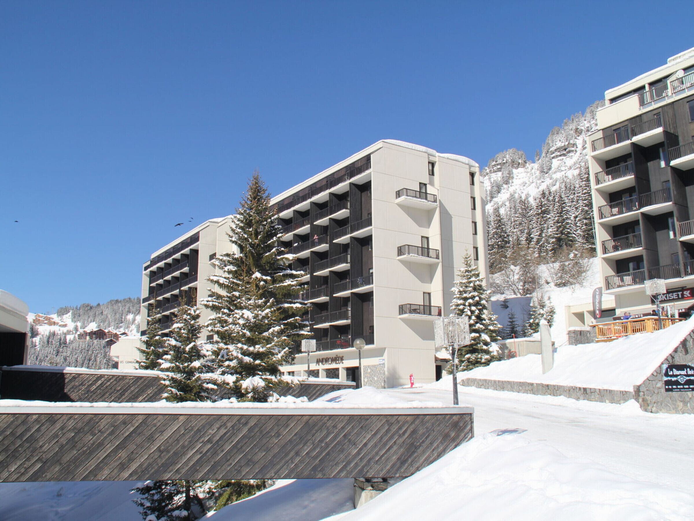 A multi-story hotel with a modern design, featuring balconies on each floor and a ski slope in the background.