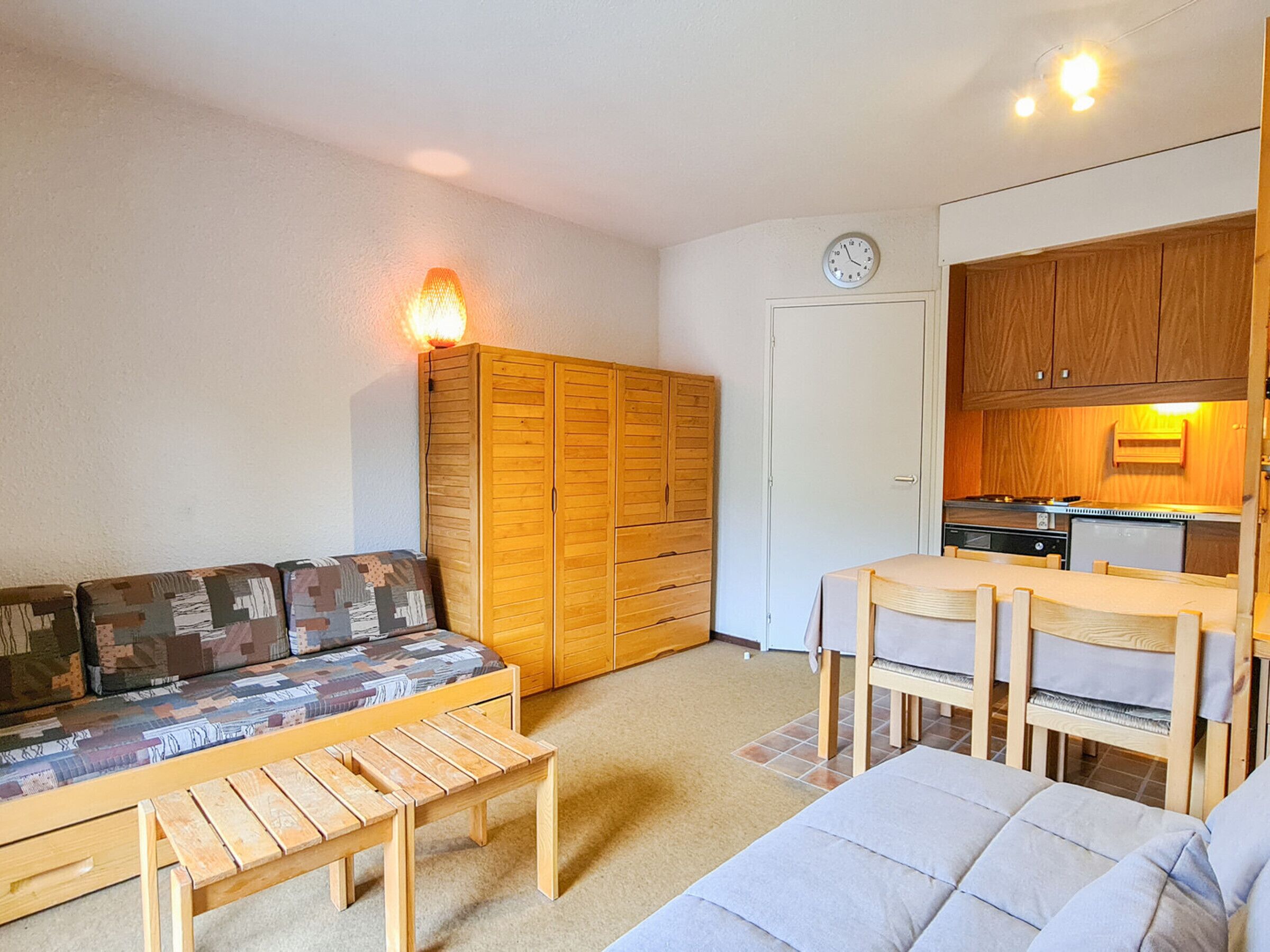A compact living space with a sofa, a small dining table, wooden cabinets, and a kitchenette.