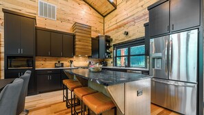 A modern kitchen with wooden walls, a stainless steel refrigerator, and a bar area with stools. - Riverfront Modern Cabin/Pickle Ball/Slide/Shuffleboard/Outdoor Shower (Eagletown)
