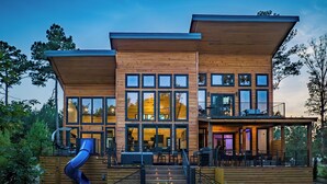 A modern wooden house with a large deck, a slide, and multiple windows. - Riverfront Modern Cabin/Pickle Ball/Slide/Shuffleboard/Outdoor Shower (Eagletown)