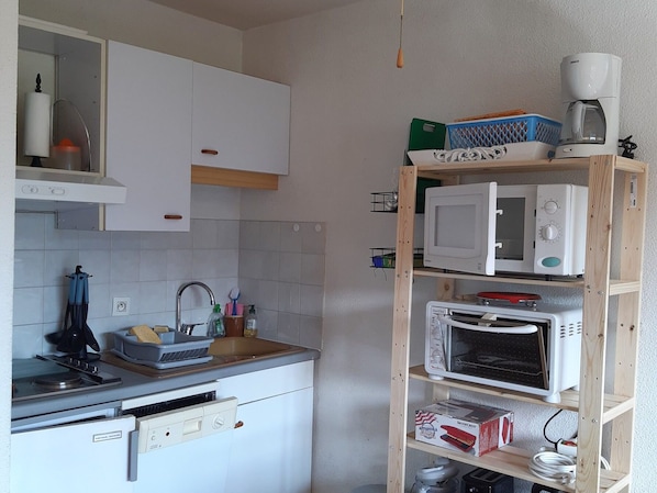 A compact kitchen with white cabinets, a built-in microwave, a toaster, and a coffee maker on a wooden shelf.