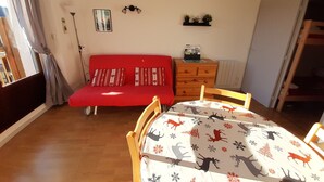 A room with a red sofa, a wooden dresser, a dining table with a deer pattern tablecloth, and a window with curtains. - Studio cabin in Villard-de-Lans, south balcony, parking, ski locker (Villard-de-Lans)