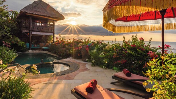 Zona junto a la piscina con una estructura de techo de paja, sillas de descanso y un parasol decorativo.