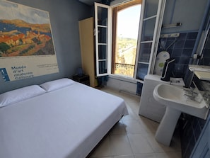 A hotel room with a bed, a bathroom with a sink and mirror, a window with a view, and a poster on the wall.