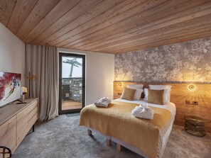 A bedroom with a wooden ceiling, a bed with a beige blanket, a stone wall, and a view of a ski lift.