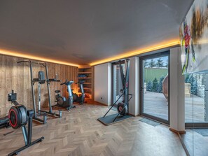 A gym with various exercise equipment, wooden walls, and a view of a snowy landscape through a glass door. - New Apartment in Courchevel - Ski-in/Ski-out with Parking (Courchevel 1850)
