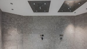 A modern shower room with grey tiled walls and ceiling, two showerheads, and recessed lighting.