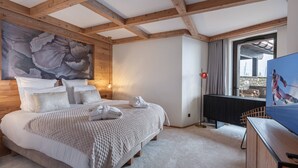 A bedroom with a large bed, wooden beams, a painting, a TV, and a view of the outside.