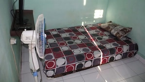 A small room with a bed, a standing fan, a television, and a power outlet. - Ekost Bayeman (Sleman)