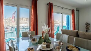 Een eetgedeelte met een tafel gedekt voor twee personen, uitzicht op de haven en een balkon met stoelen.