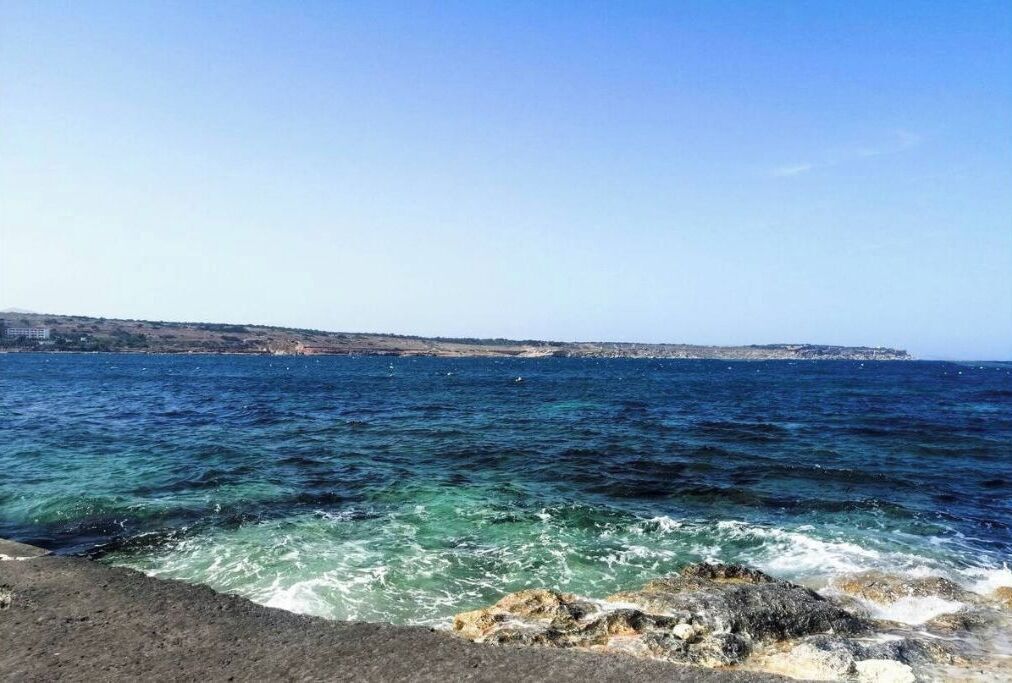 Eine Küstenansicht mit felsigem Gelände und klarem, blauem Wasser.