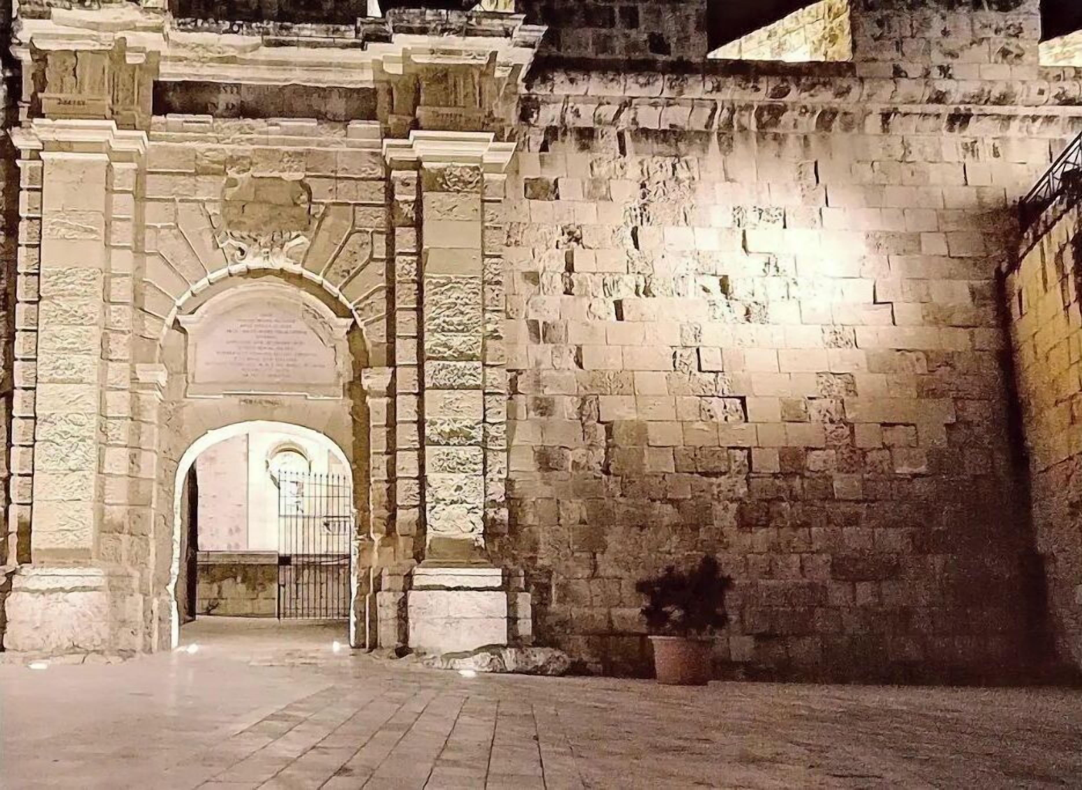 Un antiguo arco de piedra que da paso a un patio con una planta en maceta y una reja de metal.