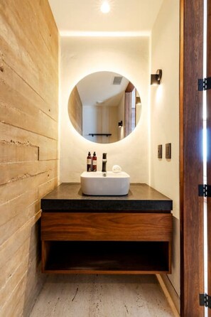 A modern bathroom with a wooden wall, a round mirror, and a white sink with toiletries.