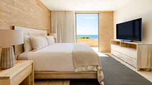 A modern bedroom with a large bed, a TV, and a view of the ocean. - Stunning Oceanview Condo (San José del Cabo)