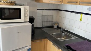Una cocina compacta equipada con microondas, refrigerador, lavamanos y tetera.