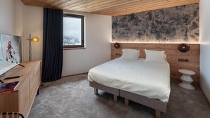 Ein Schlafzimmer mit Holzbalkendecke, einem Bett mit weißer Bettwäsche, einem Schreibtisch mit Lampe und einem Gemälde an der Wand.