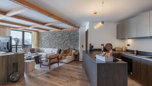 Ein modernes Interieur mit Steinwand, Holzbalken, einer Küche mit dunklen Schränken und einer Sitzecke mit Blick.
