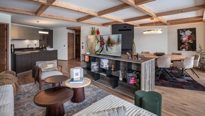 Ein geräumiger Wohnbereich mit Holzboden, einem Fernseher, einem Esstisch mit Stühlen und einer Küche im Hintergrund.