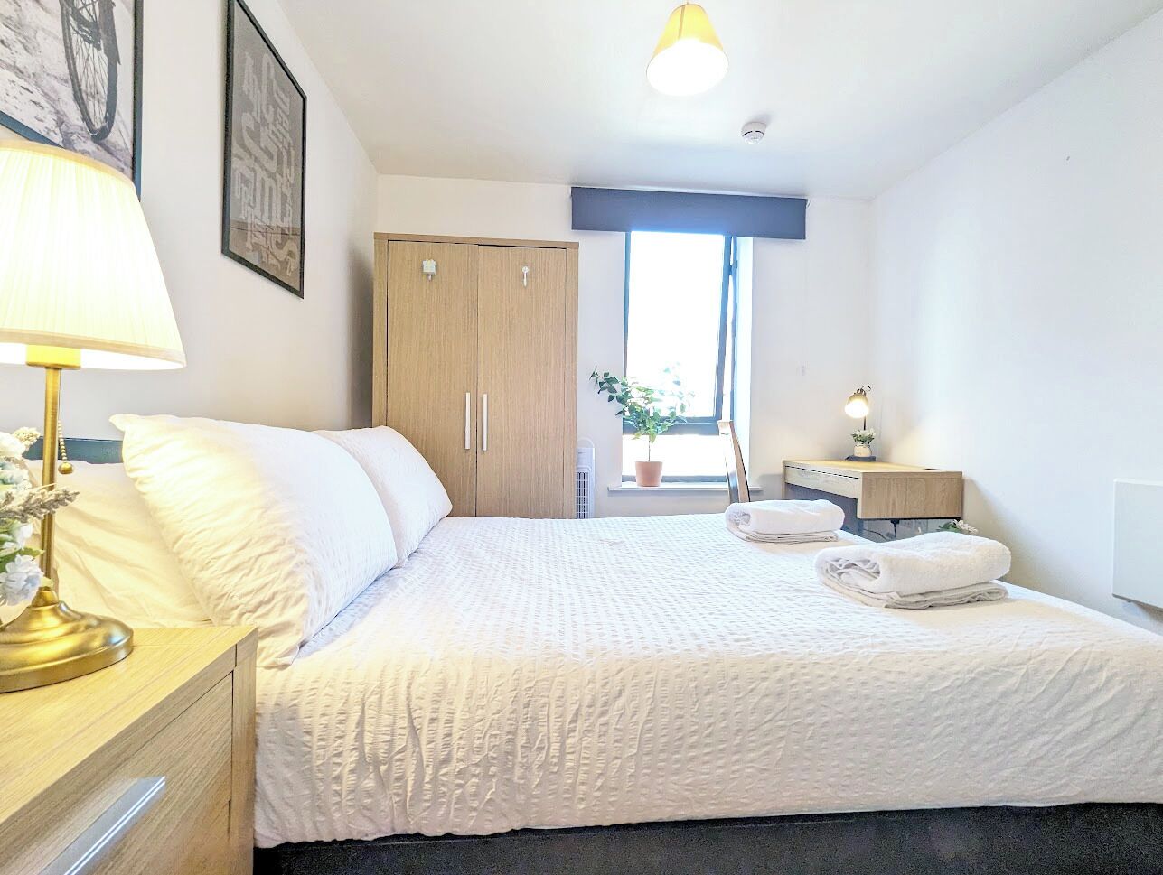 Una camera da letto ordinata con un letto, un comodino, una lampada e una finestra vista.