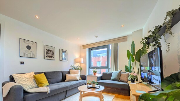 A modern living room with a grey sofa, a round coffee table, and a TV on a wooden stand.