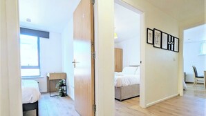 A modern, well-lit room with a wooden floor, a bed, a bedside table, and a window.