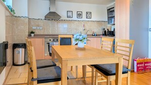 A modern kitchen with a dining table, chairs, a stainless steel trash bin, and a built-in oven.