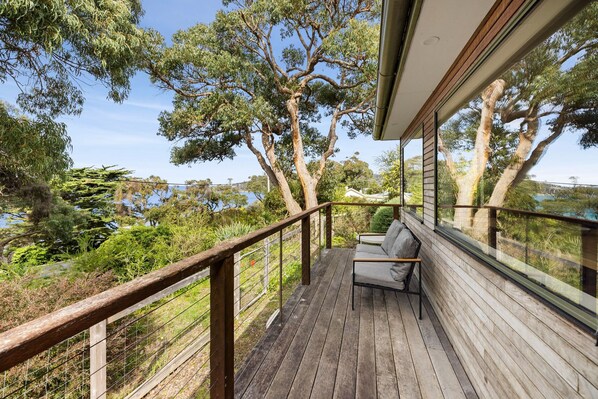 A wooden deck with a metal railing, a sofa, and a view of trees and a body of water.