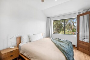 Ein Schlafzimmer mit einem Bett, einem Nachttisch, einer Lampe und einem Fenster mit Vorhängen.