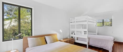 A bedroom with a large window, a bed with a wooden headboard, a nightstand, and a white bunk bed.