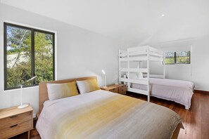 A bedroom with a large window, a bed with a wooden headboard, a nightstand, and a white bunk bed.