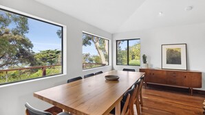 A modern dining area with a wooden table, chairs, and a view of trees through large windows. - Chatby House filtered views of the ocean (Lorne)