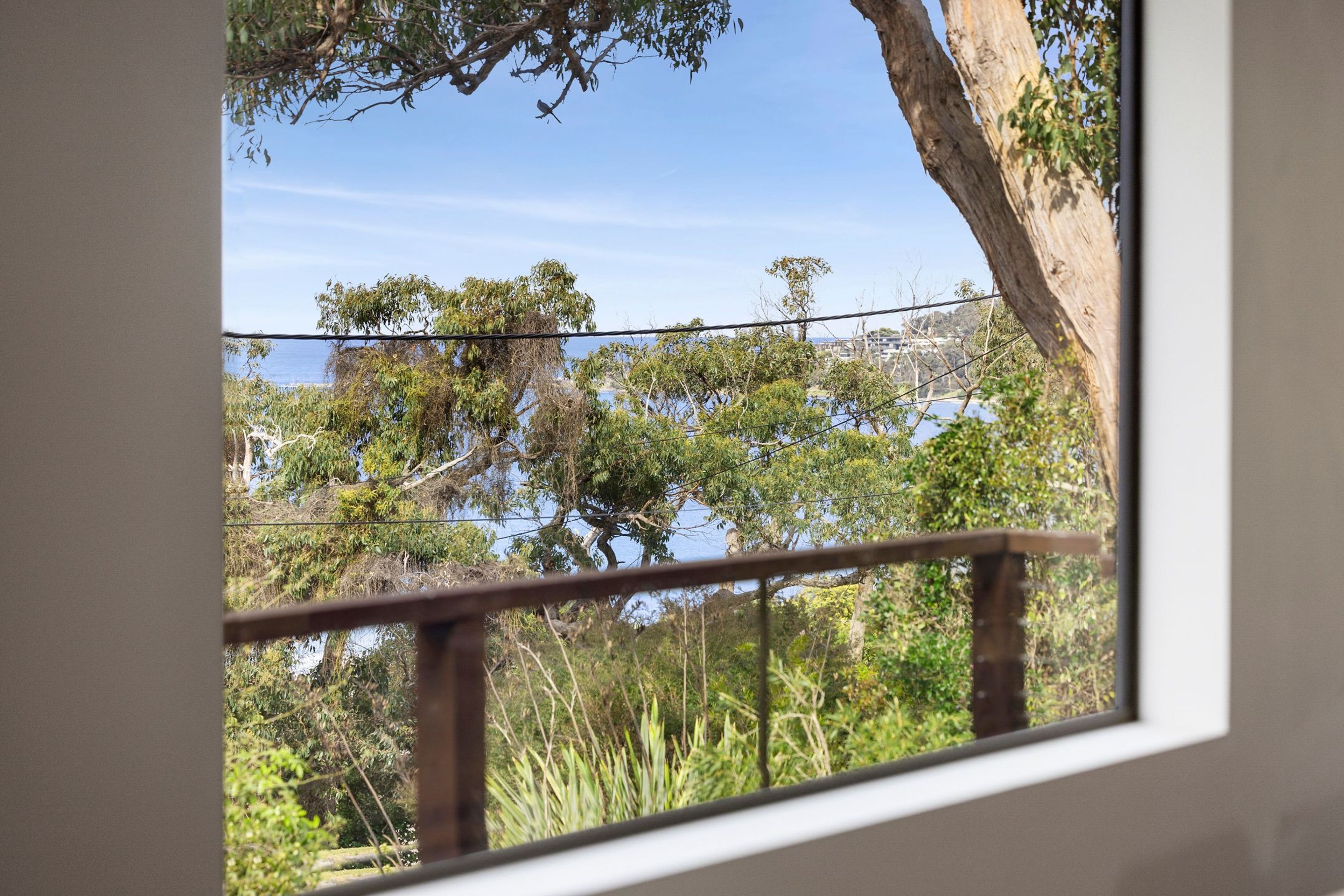A view through a window with a wooden railing, overlooking a natural landscape with trees and a body of water.