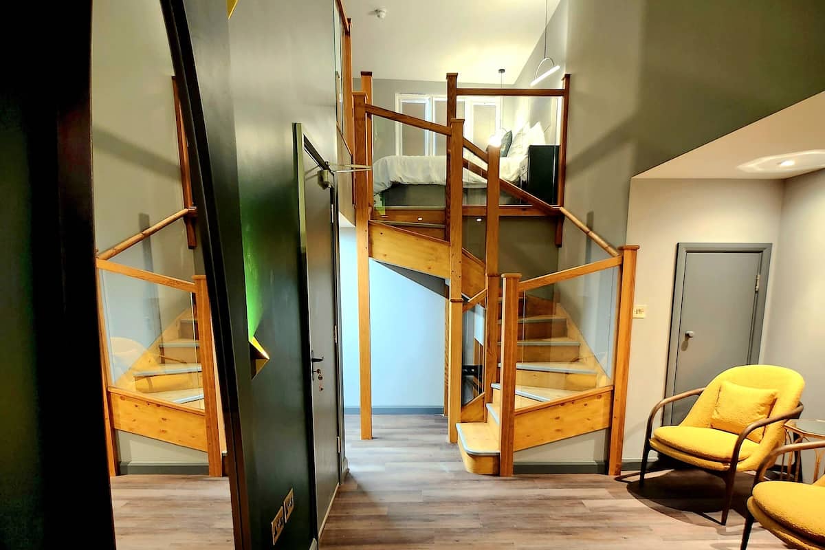 Un interior moderno con una escalera de madera, un sillón amarillo y vista a un dormitorio.