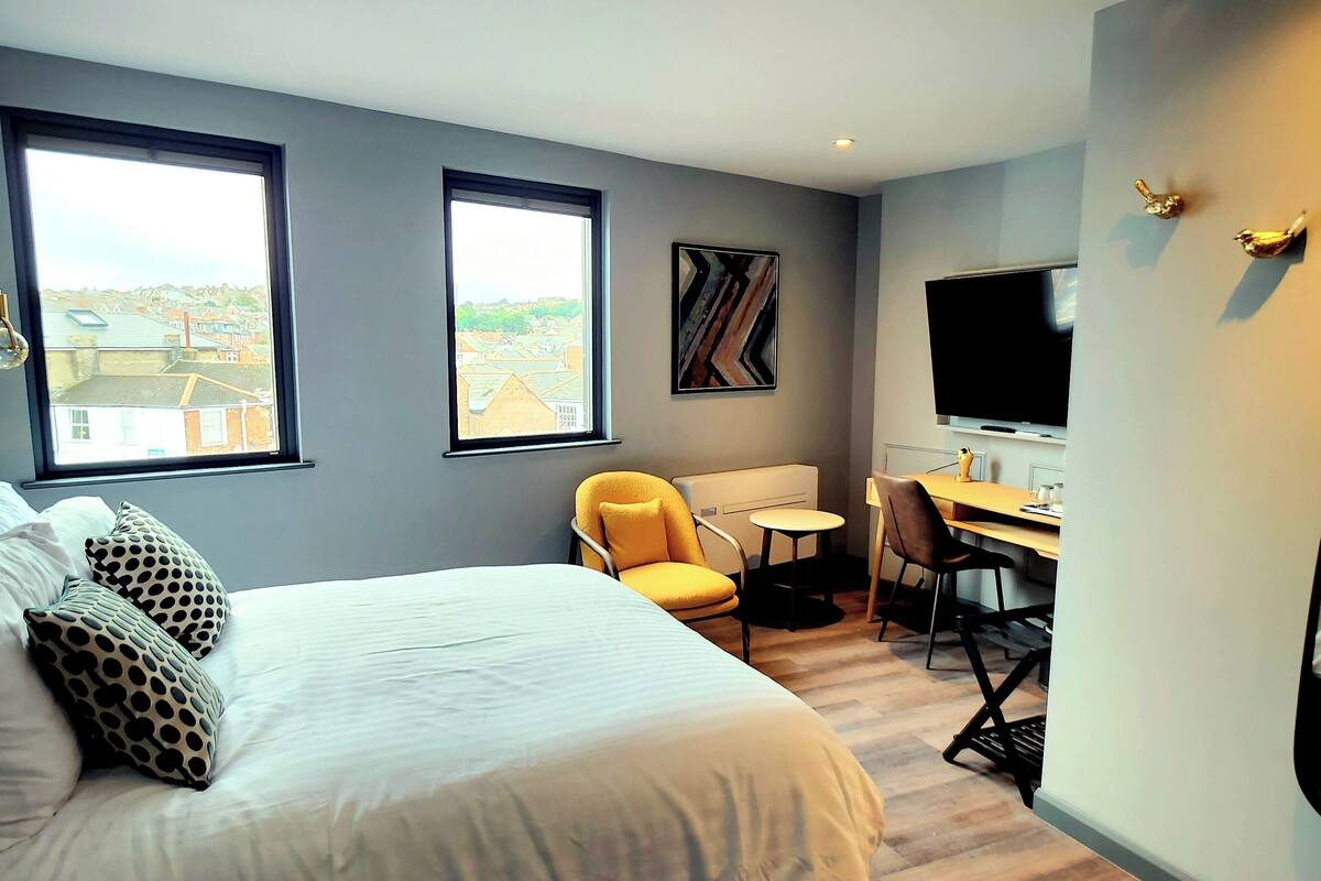 Un dormitorio con una cama, un escritorio, una silla, un televisor y dos ventanas.
