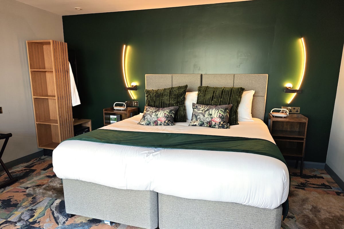 Una cama grande con cabecera, dos mesitas de noche, un armario de madera y una alfombra estampada.