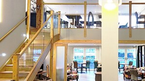 A multi-level interior with a wooden staircase, seating areas, and large windows offering views.
